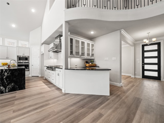 kitchen featuring light wood-type flooring, appliances with stainless steel finishes, white cabinetry, and wall chimney exhaust hood