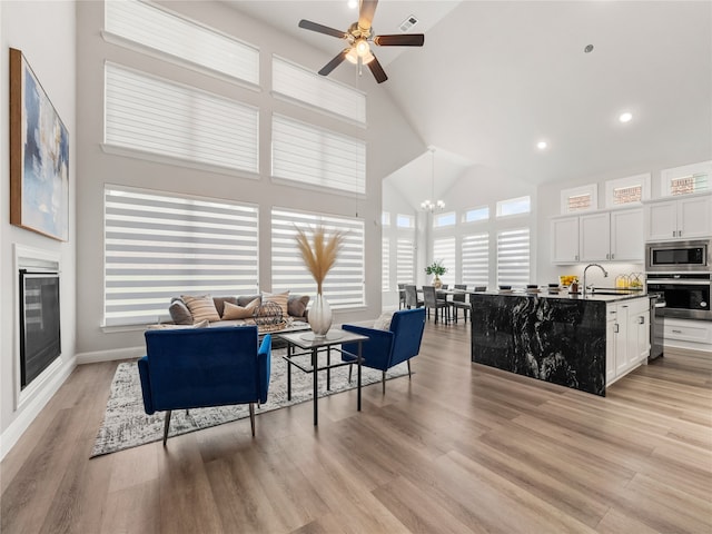 living room featuring high vaulted ceiling, sink, ceiling fan, and light hardwood / wood-style floors