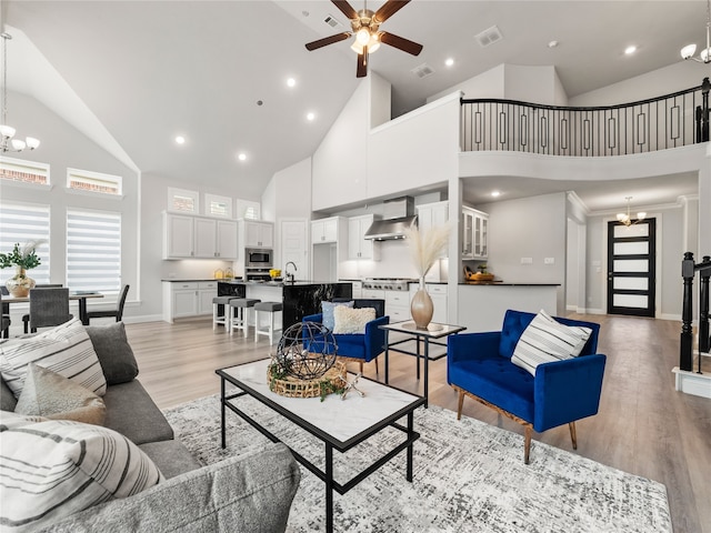 living room with ceiling fan with notable chandelier, high vaulted ceiling, and light hardwood / wood-style flooring