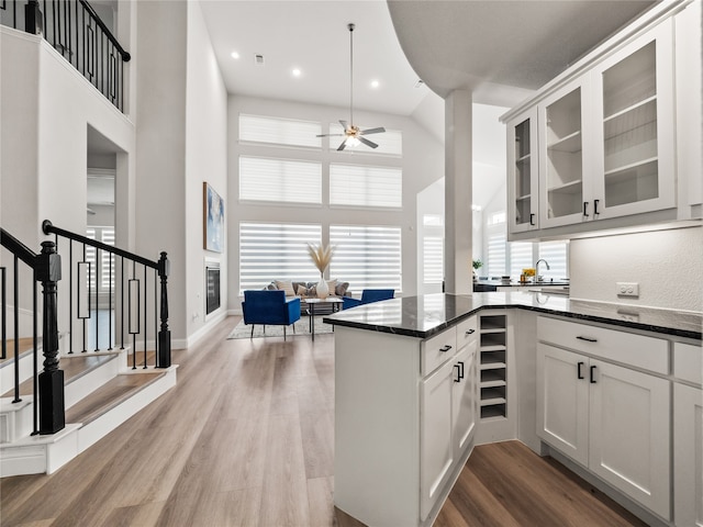 kitchen featuring dark wood-type flooring, ceiling fan, white cabinetry, dark stone countertops, and a towering ceiling