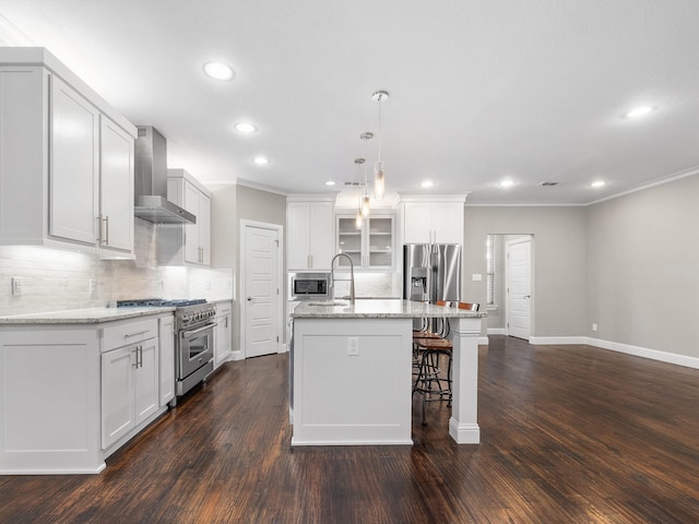 kitchen with a center island with sink, dark wood-type flooring, stainless steel appliances, and wall chimney range hood