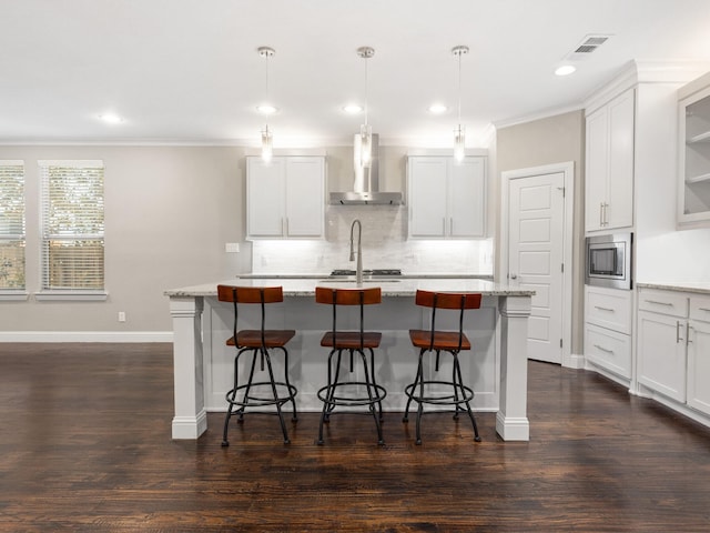 kitchen featuring an island with sink, dark wood-type flooring, stainless steel appliances, and wall chimney exhaust hood