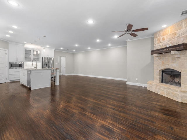 unfurnished living room with a fireplace, crown molding, dark wood-type flooring, sink, and ceiling fan