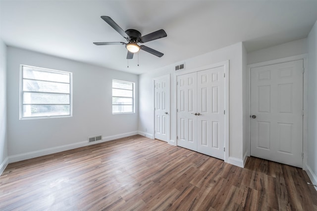 unfurnished bedroom with dark hardwood / wood-style flooring, multiple closets, ceiling fan, and multiple windows