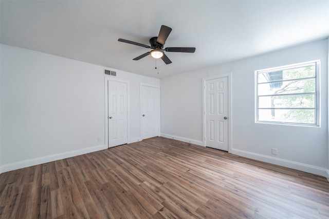 unfurnished bedroom with ceiling fan, wood-type flooring, and multiple closets