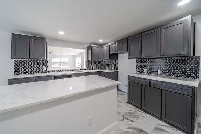 kitchen featuring backsplash, kitchen peninsula, sink, gray cabinets, and light stone counters