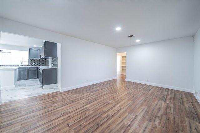 unfurnished living room with ceiling fan, sink, and light hardwood / wood-style flooring