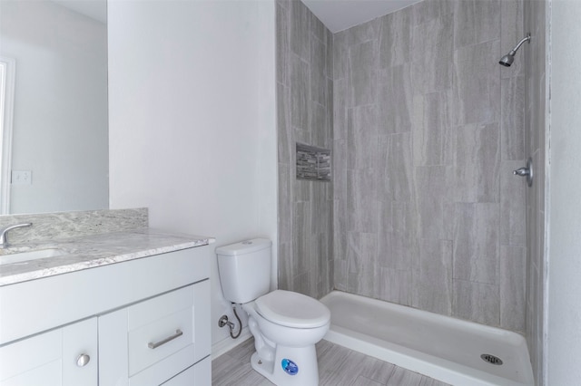 bathroom with vanity, toilet, a tile shower, and hardwood / wood-style floors