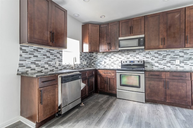 kitchen with appliances with stainless steel finishes, dark stone countertops, and hardwood / wood-style flooring