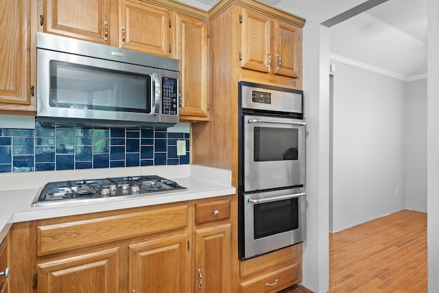 kitchen with crown molding, stainless steel appliances, light hardwood / wood-style flooring, and backsplash