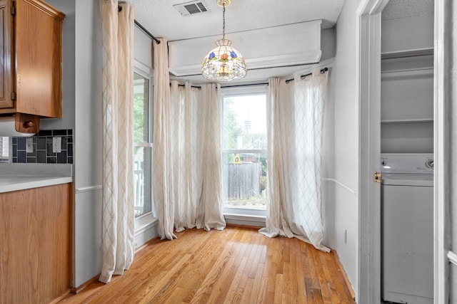 unfurnished dining area with a textured ceiling, light hardwood / wood-style flooring, a notable chandelier, and washer / clothes dryer