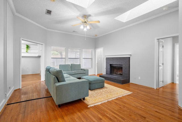 living room with a skylight, hardwood / wood-style flooring, a fireplace, ceiling fan, and a textured ceiling