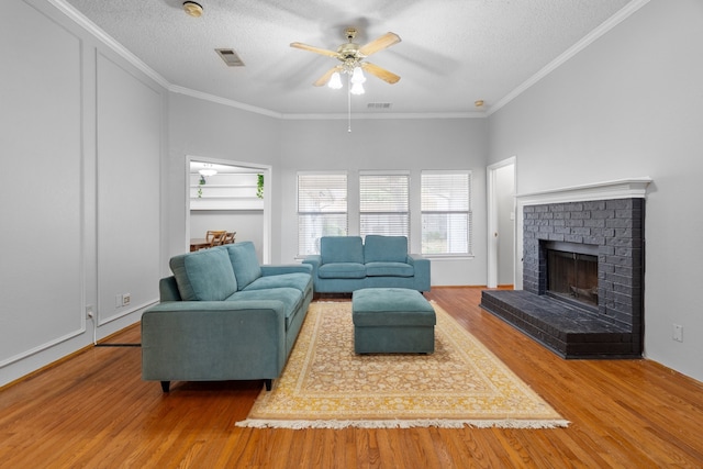 living room with a textured ceiling, ceiling fan, wood-type flooring, and a brick fireplace