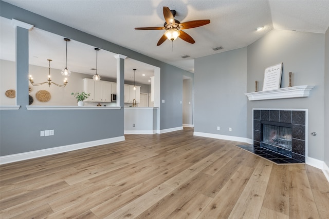 unfurnished living room with a textured ceiling, ceiling fan with notable chandelier, light hardwood / wood-style floors, lofted ceiling, and a tiled fireplace