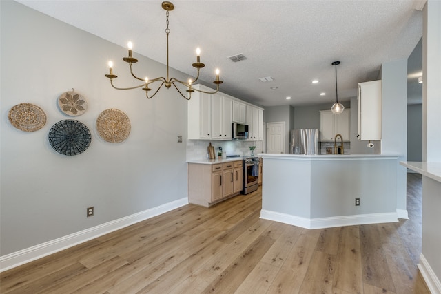 kitchen with white cabinets, sink, appliances with stainless steel finishes, decorative light fixtures, and light hardwood / wood-style floors