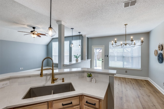 kitchen featuring decorative light fixtures, vaulted ceiling, sink, and light hardwood / wood-style flooring