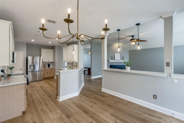 kitchen featuring hanging light fixtures, light hardwood / wood-style flooring, stainless steel fridge, vaulted ceiling, and white cabinets