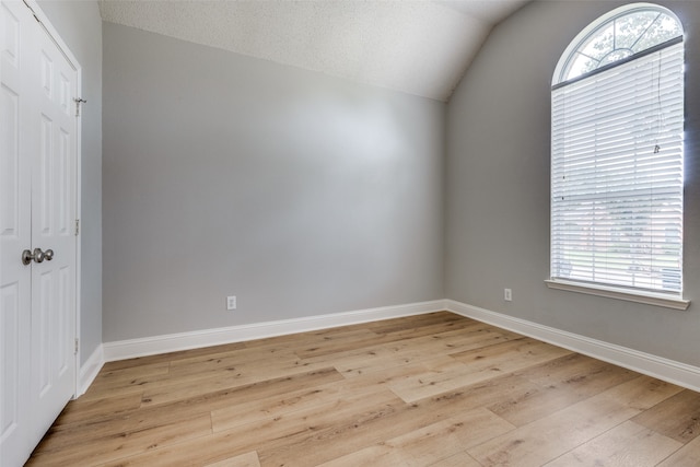 spare room with light wood-type flooring, a textured ceiling, and vaulted ceiling