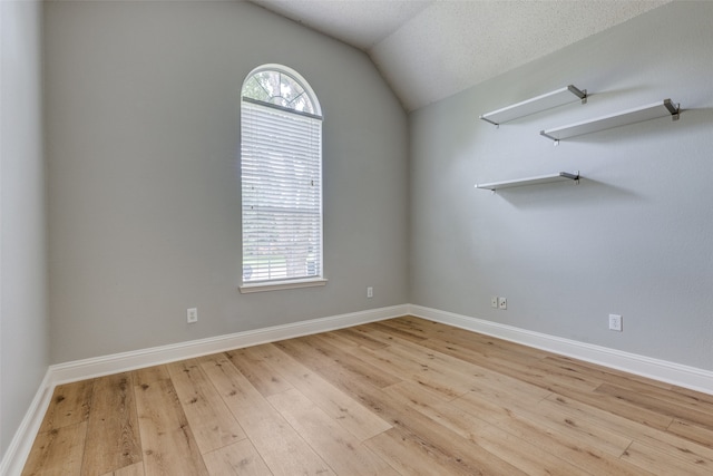 empty room with a textured ceiling, vaulted ceiling, and light wood-type flooring