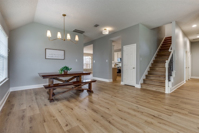 dining area featuring a textured ceiling, a chandelier, light hardwood / wood-style floors, and lofted ceiling