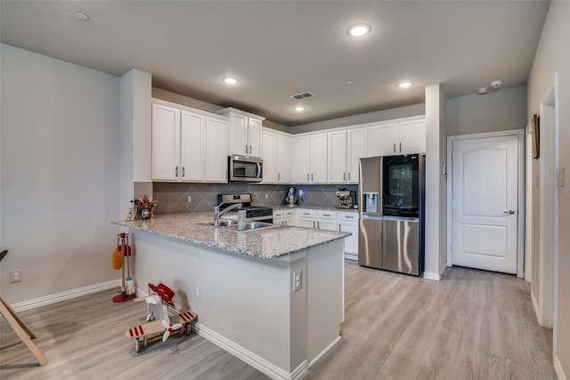 kitchen featuring light stone countertops, light hardwood / wood-style flooring, backsplash, appliances with stainless steel finishes, and white cabinets