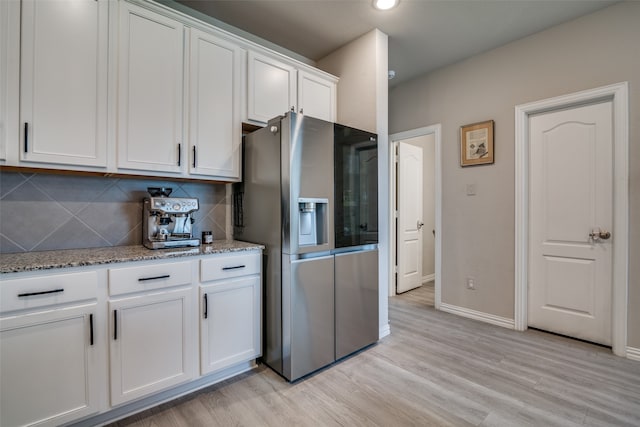 kitchen featuring stainless steel fridge, white cabinetry, backsplash, light stone counters, and light hardwood / wood-style floors