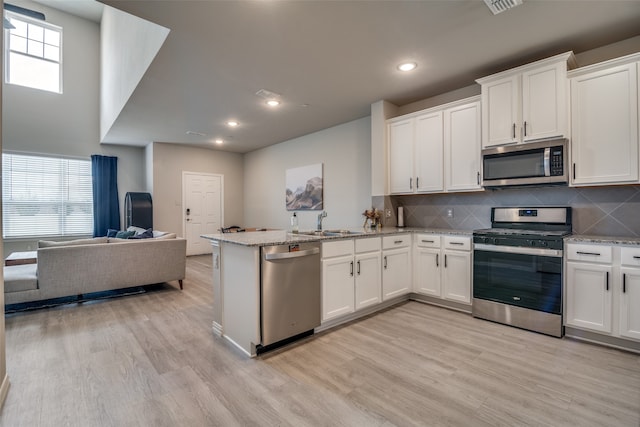 kitchen with light wood-type flooring, appliances with stainless steel finishes, light stone countertops, white cabinetry, and kitchen peninsula