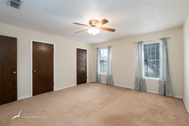 unfurnished bedroom with a textured ceiling, ceiling fan, light colored carpet, and two closets