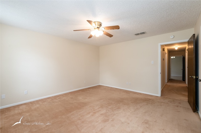 empty room with ceiling fan, light colored carpet, and a textured ceiling