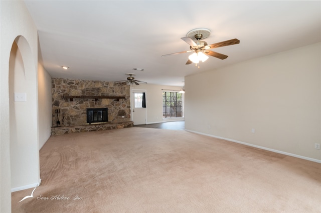 unfurnished living room featuring carpet floors, a stone fireplace, and ceiling fan