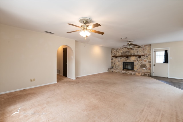 unfurnished living room featuring carpet flooring, a stone fireplace, and ceiling fan