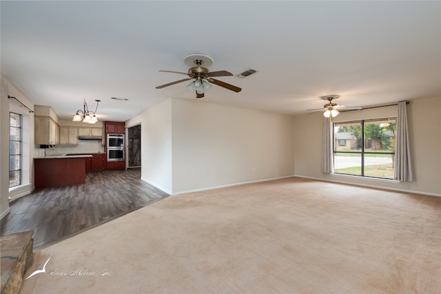 unfurnished living room with ceiling fan with notable chandelier and dark colored carpet