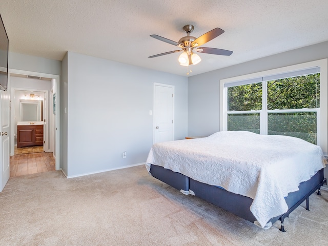 bedroom with ensuite bath, light colored carpet, ceiling fan, and a textured ceiling