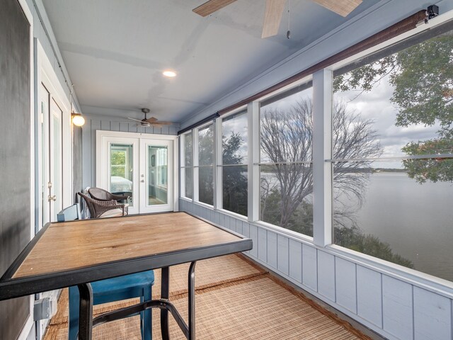 sunroom / solarium with a water view, ceiling fan, and french doors