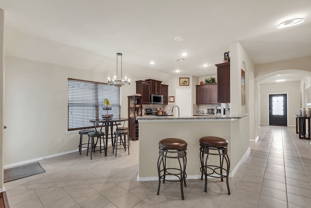 kitchen featuring light stone countertops, electric range oven, a kitchen breakfast bar, kitchen peninsula, and pendant lighting