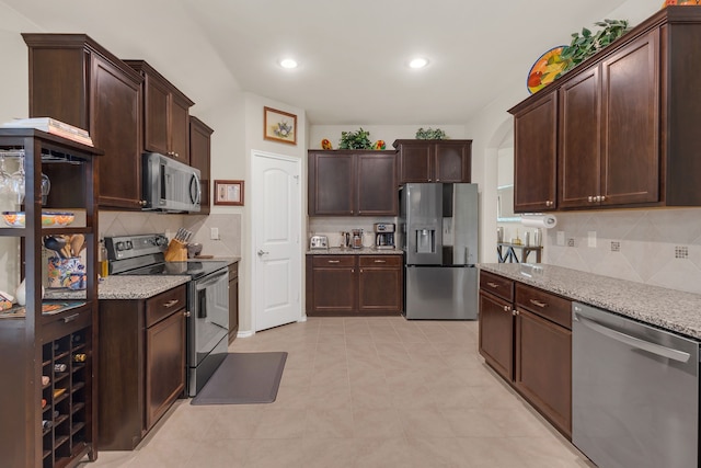 kitchen with appliances with stainless steel finishes, light stone counters, dark brown cabinets, and tasteful backsplash