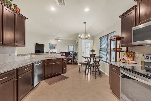 kitchen with ceiling fan with notable chandelier, appliances with stainless steel finishes, light stone countertops, sink, and tasteful backsplash