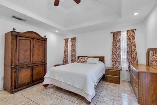 bedroom with ceiling fan, a tray ceiling, and light tile patterned flooring