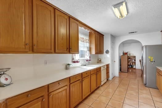 kitchen with white dishwasher, stainless steel refrigerator, a textured ceiling, and light tile patterned flooring