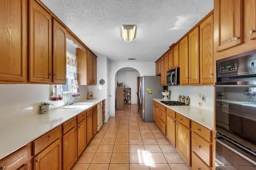 kitchen with a textured ceiling, stainless steel appliances, sink, and light tile patterned floors