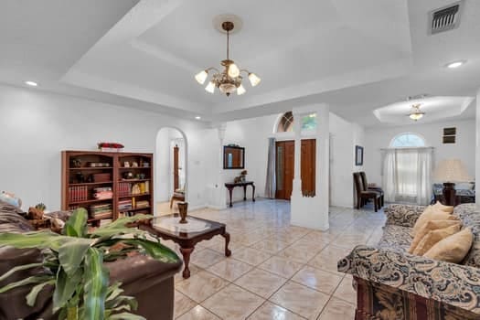 living room with a chandelier, a tray ceiling, and light tile patterned flooring