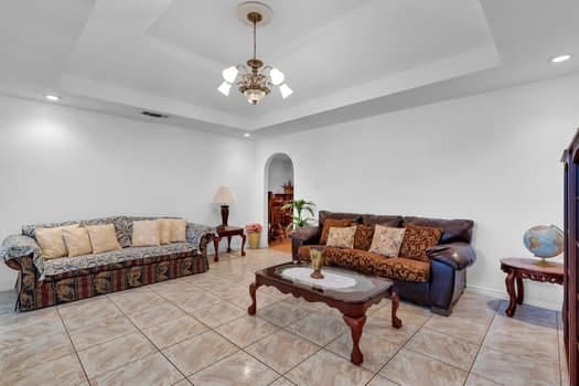 tiled living room with a chandelier and a raised ceiling