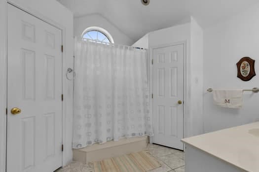 bathroom with tile patterned flooring, a shower with shower curtain, vaulted ceiling, and vanity