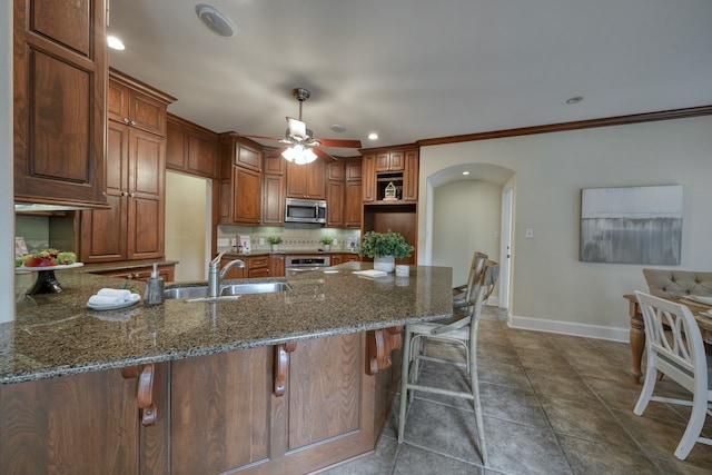 kitchen with backsplash, appliances with stainless steel finishes, dark stone counters, ceiling fan, and a kitchen bar