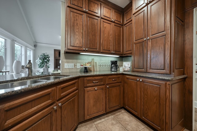 kitchen featuring dark stone countertops, light tile patterned floors, sink, decorative backsplash, and ornamental molding