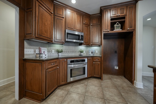 kitchen with stainless steel appliances, light tile patterned flooring, dark stone counters, and tasteful backsplash