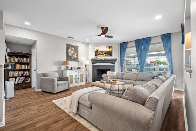 living room featuring ceiling fan, wood-type flooring, and a brick fireplace