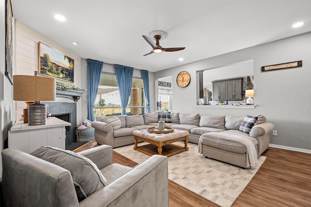 living room featuring light hardwood / wood-style flooring, ceiling fan, and a tiled fireplace