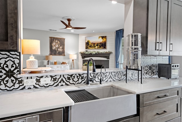 kitchen with backsplash, sink, ceiling fan, gray cabinets, and light stone countertops