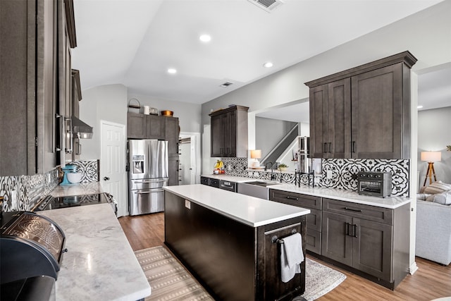 kitchen featuring a center island, tasteful backsplash, stainless steel fridge, light hardwood / wood-style floors, and vaulted ceiling